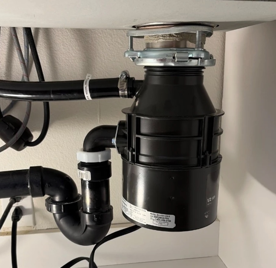 Garbage disposal unit mounted under a kitchen sink with drain pipes and power cord