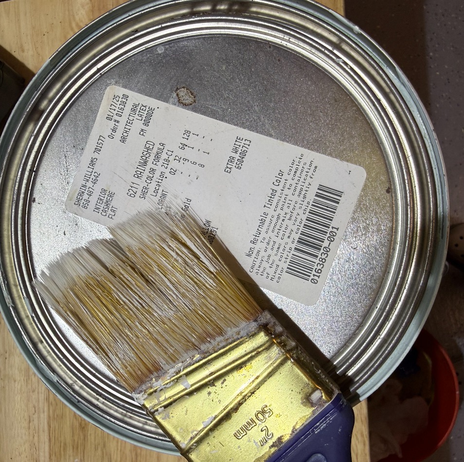 Paintbrush resting on an open can of interior wall paint