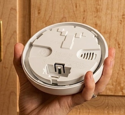 Hand holding a smoke detector removed from its ceiling mount