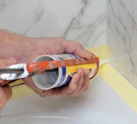 Applying a fresh bead of caulk along a bathtub edge with a caulk gun and painter's tape