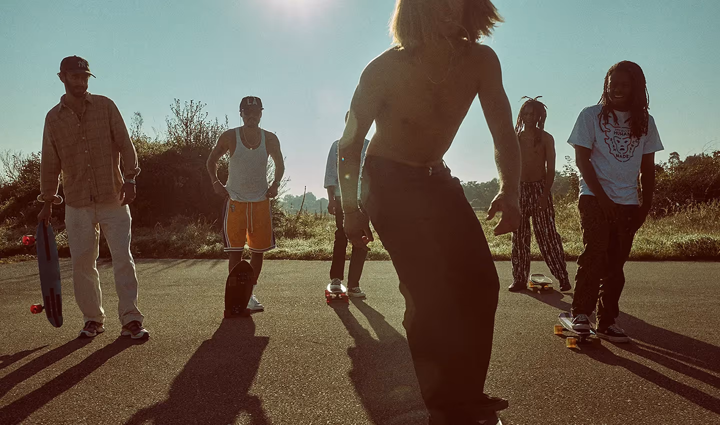 Gruppe von Jugendlichen fährt Skateboard auf einer Straße im warmen Sonnenlicht für die BANZAI Kampagne