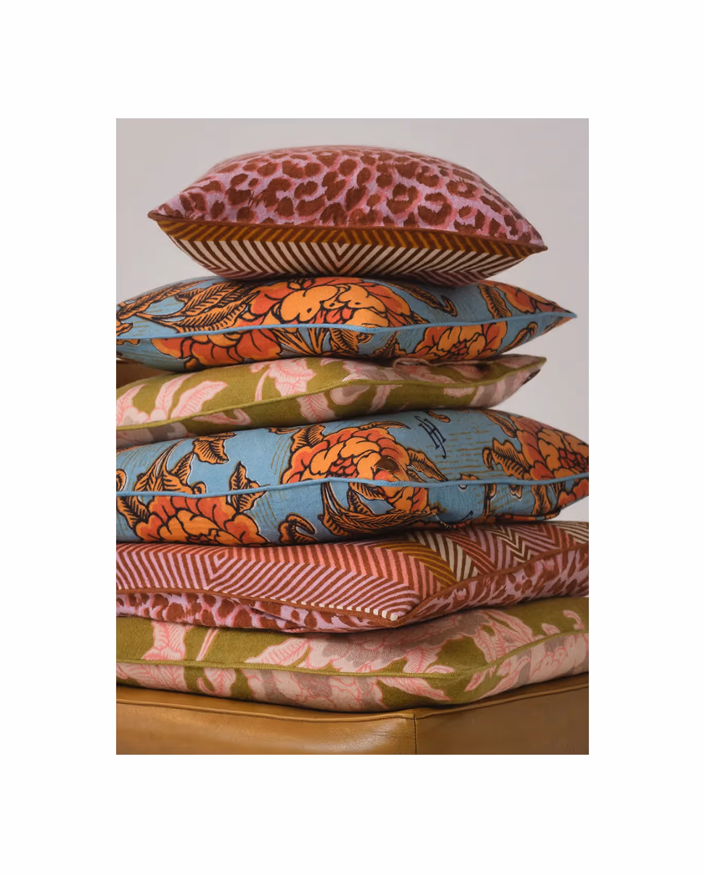 Gestapelte Kissen mit verschiedenen floralen und grafischen Mustern in Rosa-, Grün- und Blautönen