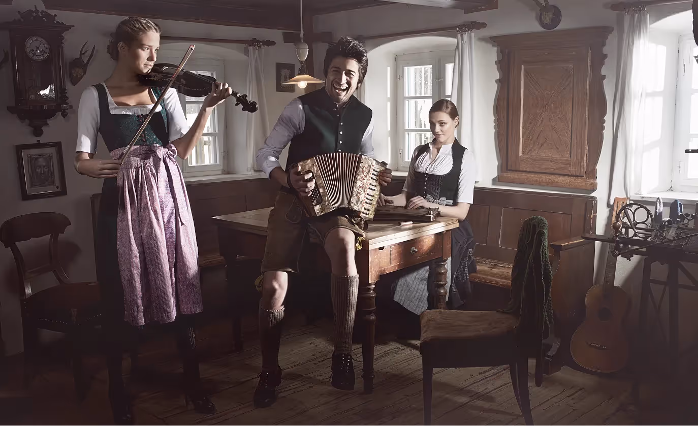 Drei Personen in traditioneller Tracht musizieren in einer rustikalen Stube im Editorial-Stil der Gottseidank Kampagne