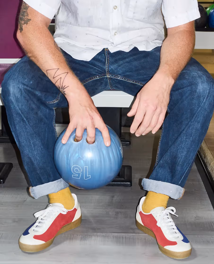 Person sitzt mit Bowlingkugel zwischen den Beinen und trägt Sneaker