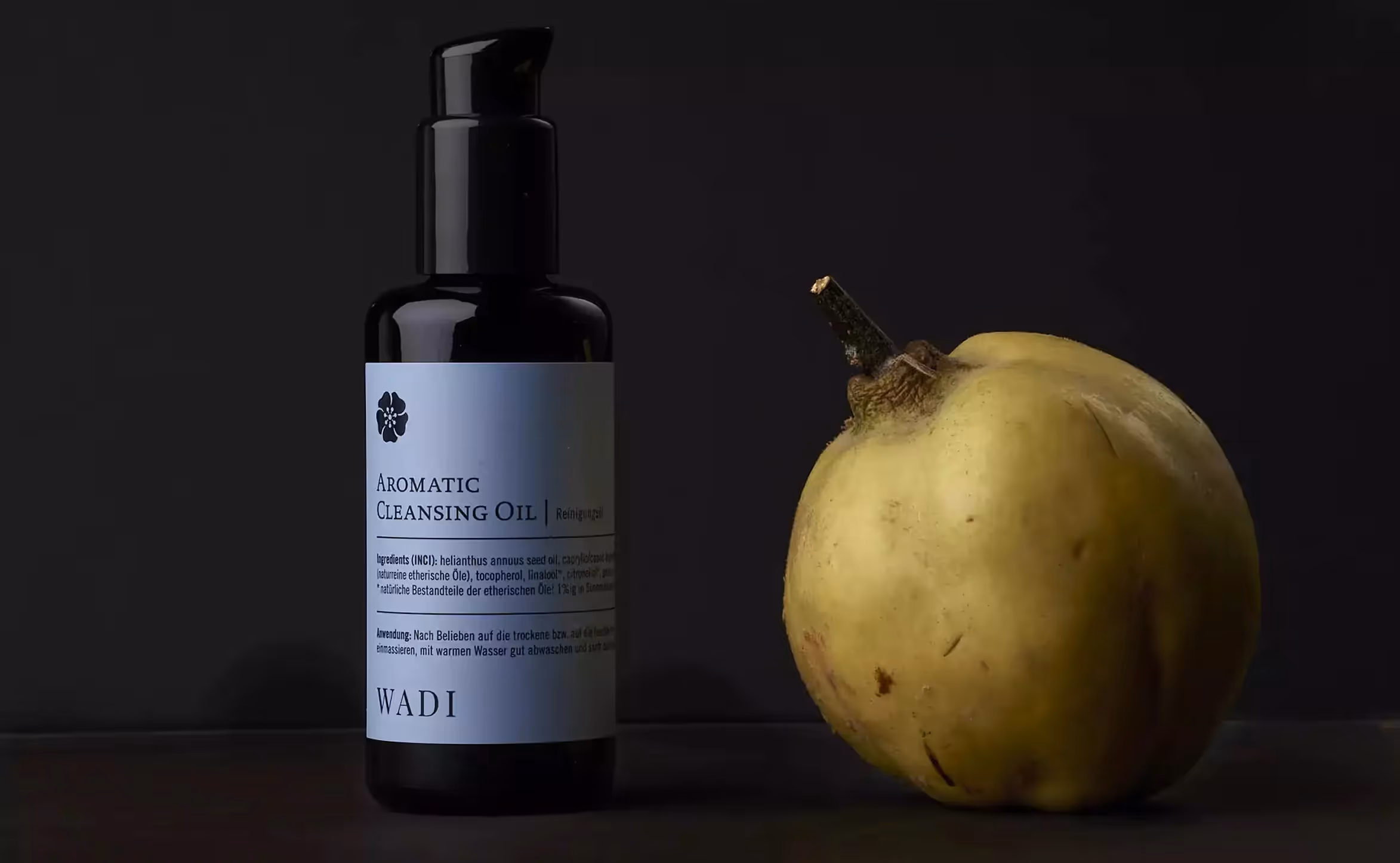 Produktflasche neben einer gelben Frucht auf dunklem Hintergrund