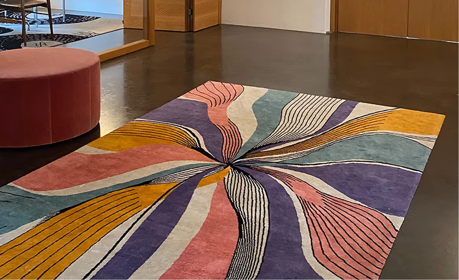 Teppich mit buntem, strahlenförmigem Muster liegt in einem Raum neben einem runden Sitzmöbel