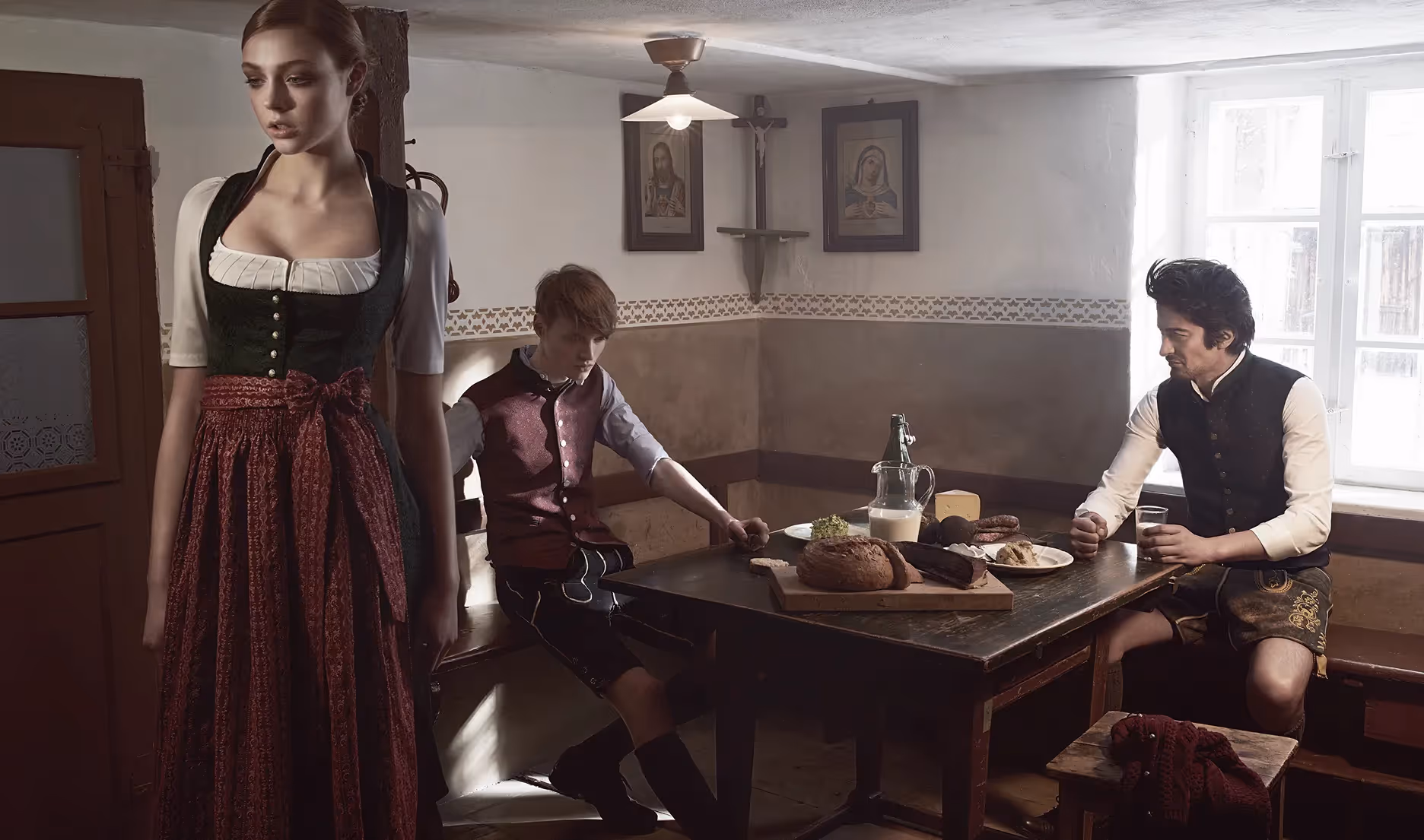 Drei Personen in Tracht sitzen an einem Holztisch in einer traditionellen Stube im warmen Licht der Gottseidank Kampagne