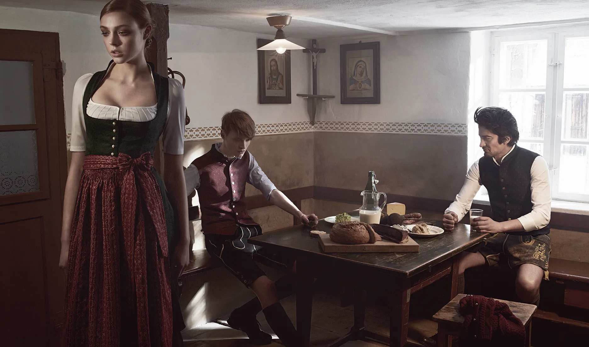 Drei Personen in Tracht sitzen an einem Holztisch in einer traditionellen Stube im warmen Licht der Gottseidank Kampagne