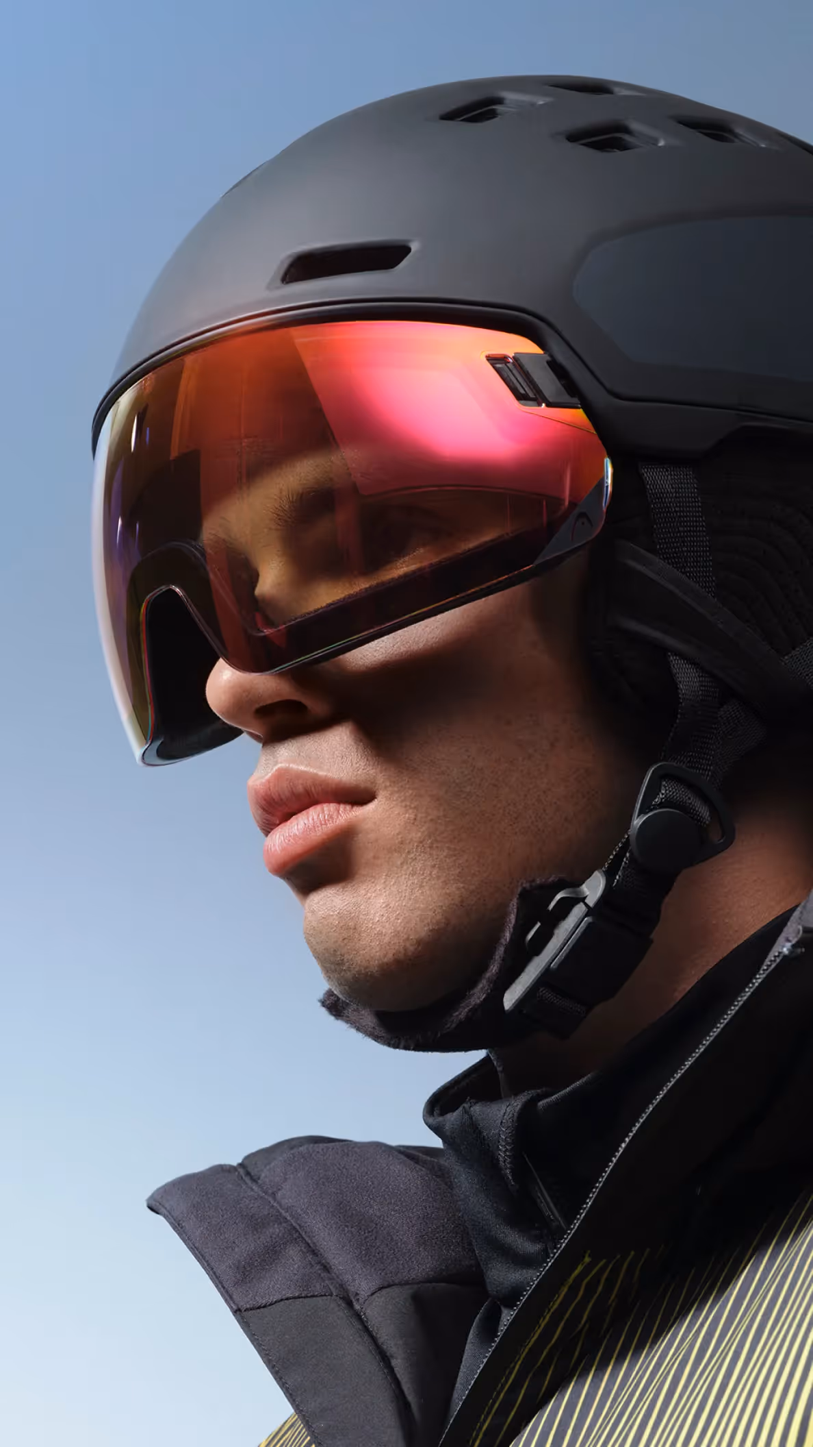 Athletischer Mann in Skiausrüstung für die HEAD Winterkampagne mit Helm und verspiegelter Skibrille vor klarem Himmel