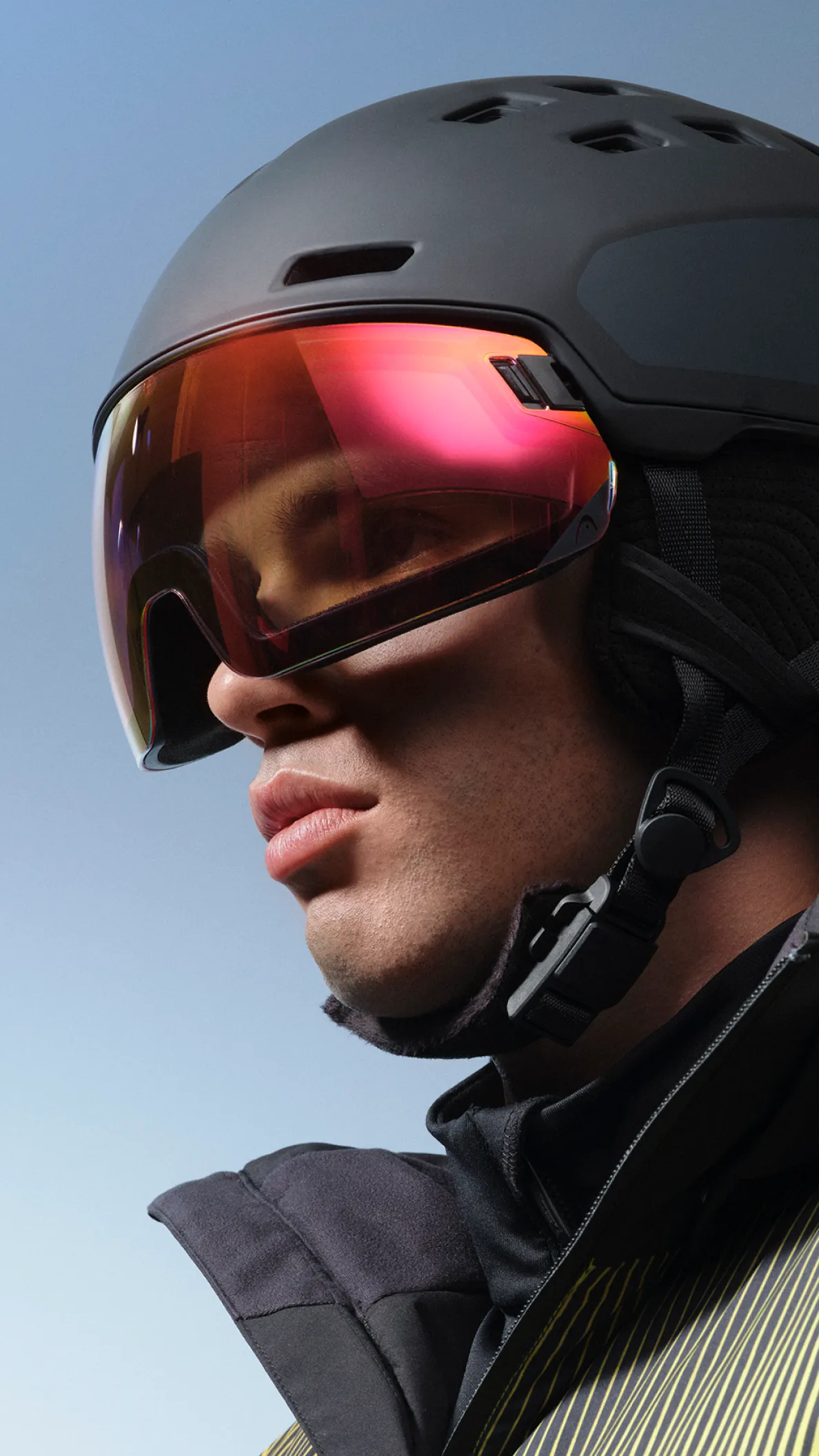 Athletischer Mann in Skiausrüstung für die HEAD Winterkampagne mit Helm und verspiegelter Skibrille vor klarem Himmel