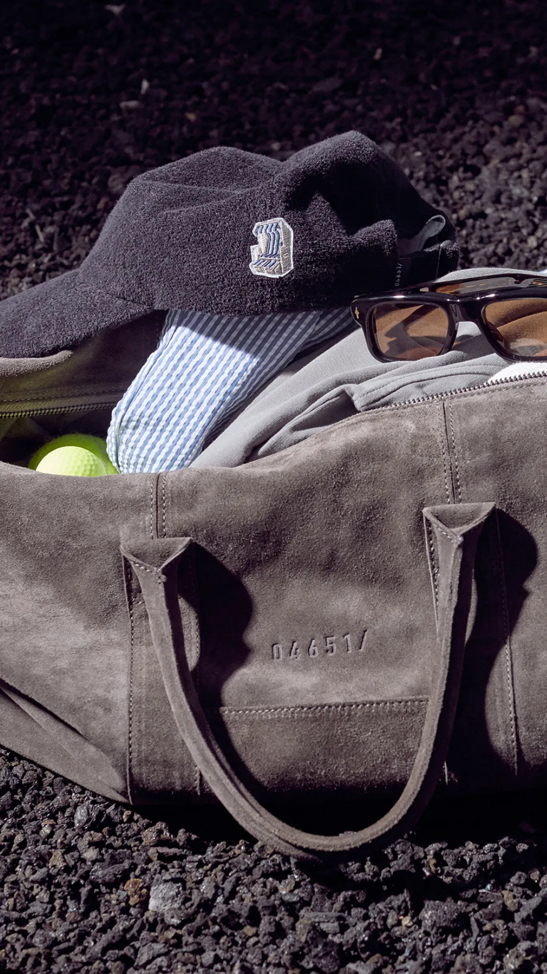 Beige Reisetasche mit Tennis-Equipment auf Sandplatz im Editorial-Stil für die 04651 Kampagne