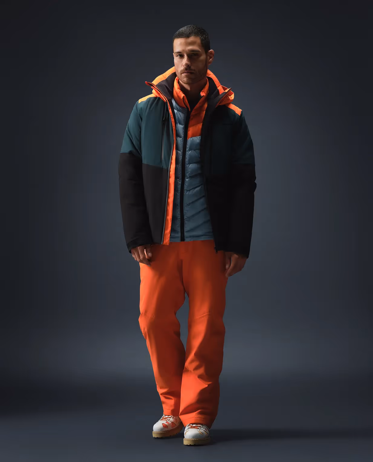 Mann in Outdoor-Outfit mit orangefarbenen Details und funktionalen Layern aus der HEAD Kollektion