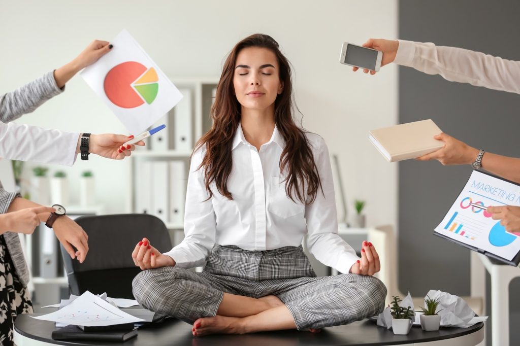 Woman meditating on her desk in an article on stress tolerance by Adam Markel