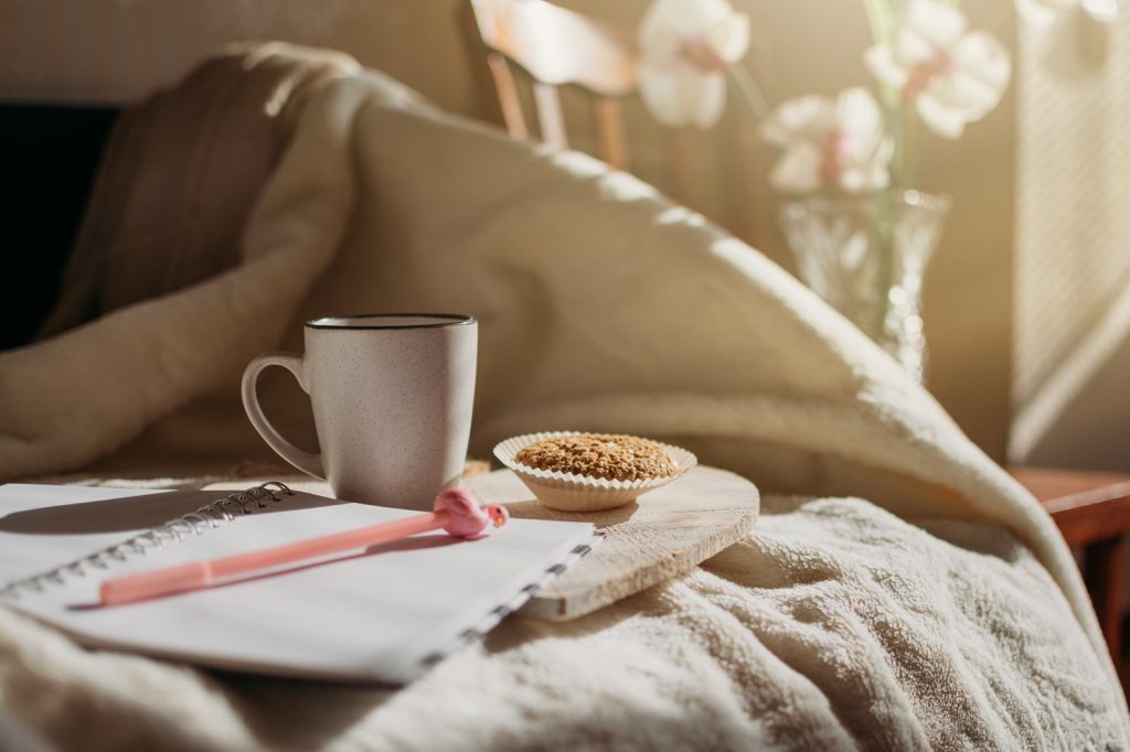 Bed with a coffee cup and journal in an article on 15 morning routine ideas by Adam Markel