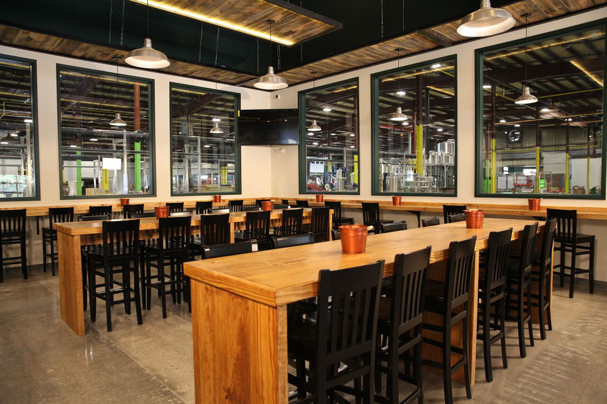 Close-up of a vibrant green pea pod hanging from a plant, surrounded by broad leaves and tendrils, set against a soft-focus, natural background.