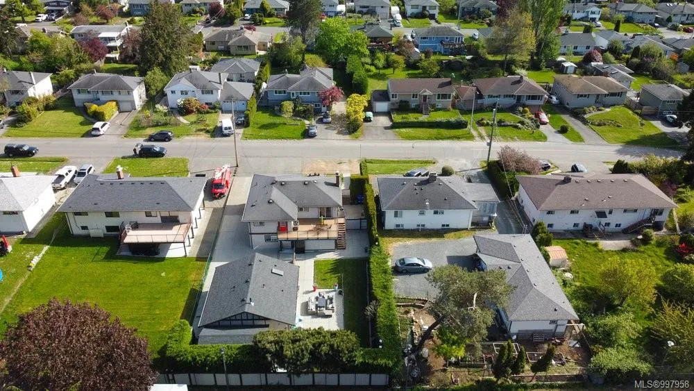 Aerial view of a residential neighborhood with single-family houses, green lawns, and parked cars along the streets. Berk Christensen Real Estate Victoria BC.