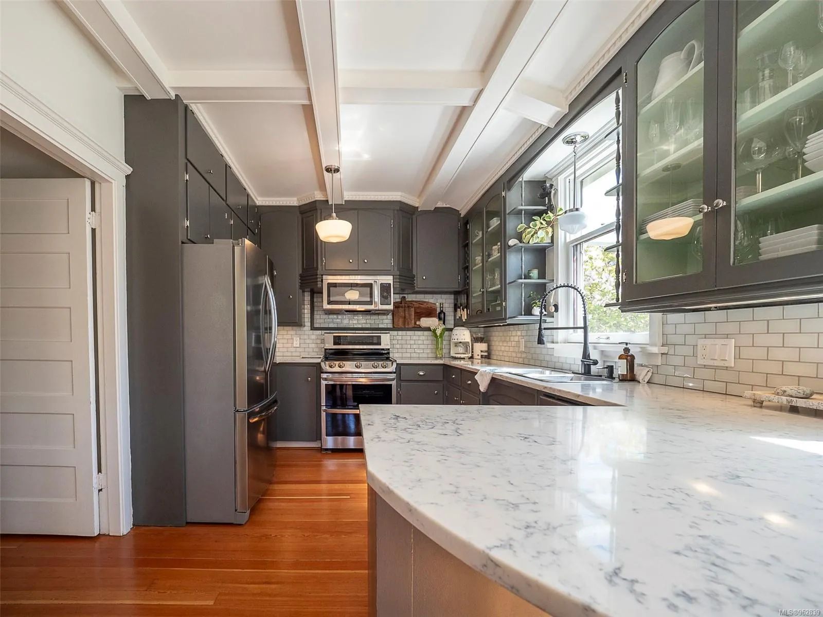 Modern kitchen with dark gray cabinets, stainless steel appliances, white subway tile backsplash, and marble countertop island. Berk Christensen Real Estate Victoria BC.