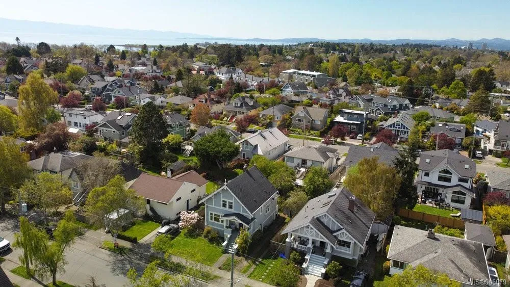 Aerial view of a suburban neighborhood with houses, green lawns, and trees under a clear sky. Berk Christensen Real Estate Victoria BC.