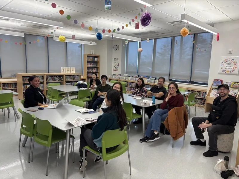 Families and staff gather around tables in a bright school library during an ACE information session