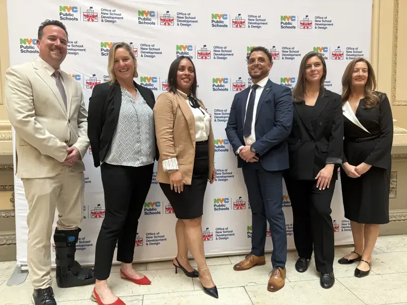 The ACE leadership team in front of the NYC Public Schools Office of New School Development and Design backdrop