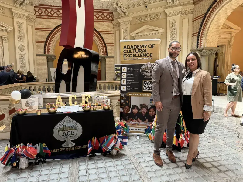Two ACE staff members smile beside the ACE table decorated with international flags
