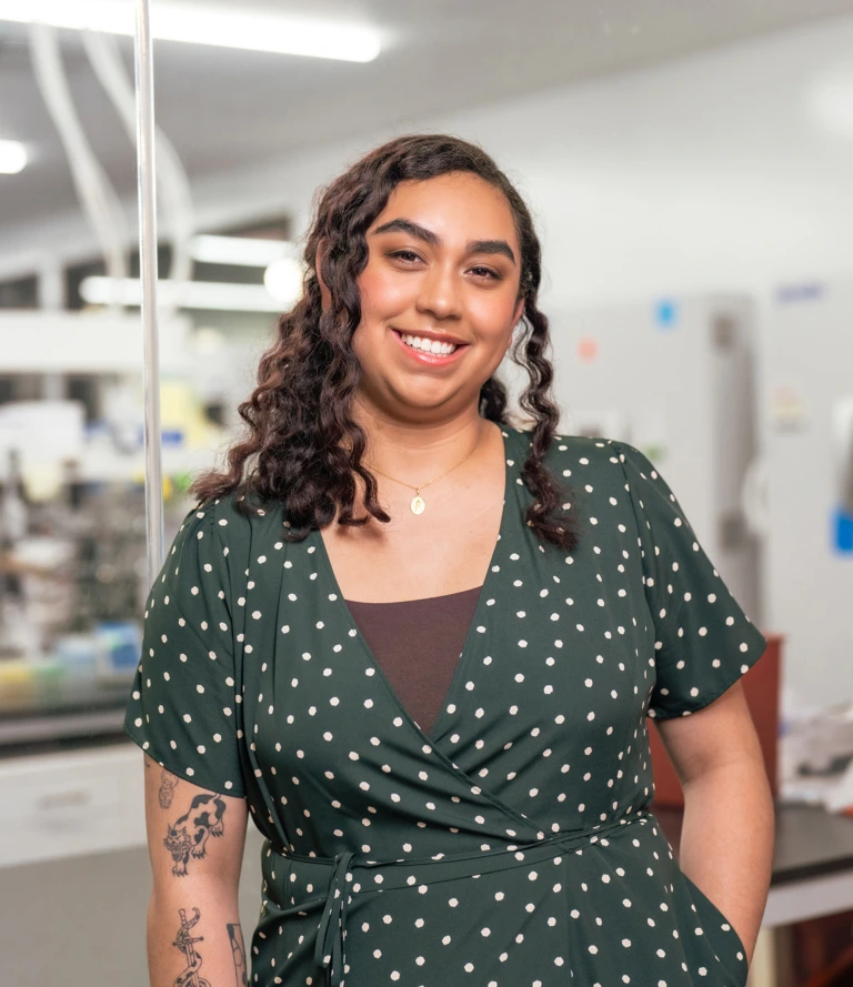 Smiling woman with curly hair wearing a green polka dot dress and standing in a bright indoor setting.