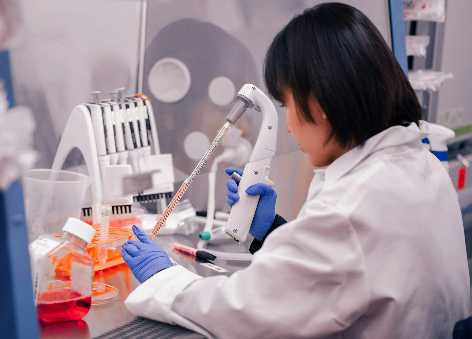 Scientist wearing blue gloves and a white lab coat using a pipette to transfer liquid in a laboratory.
