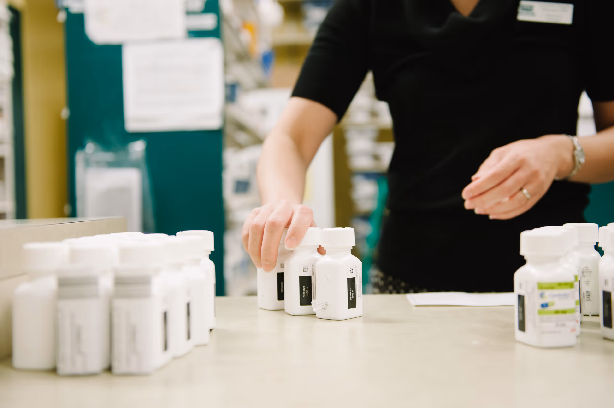 Pharmacist sorting white prescription pill bottles on a counter in a pharmacy.