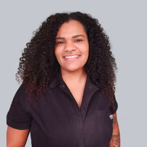 Headshot of Edidiong smiling. They have long black curly hair with lighter ends and a nose ring.