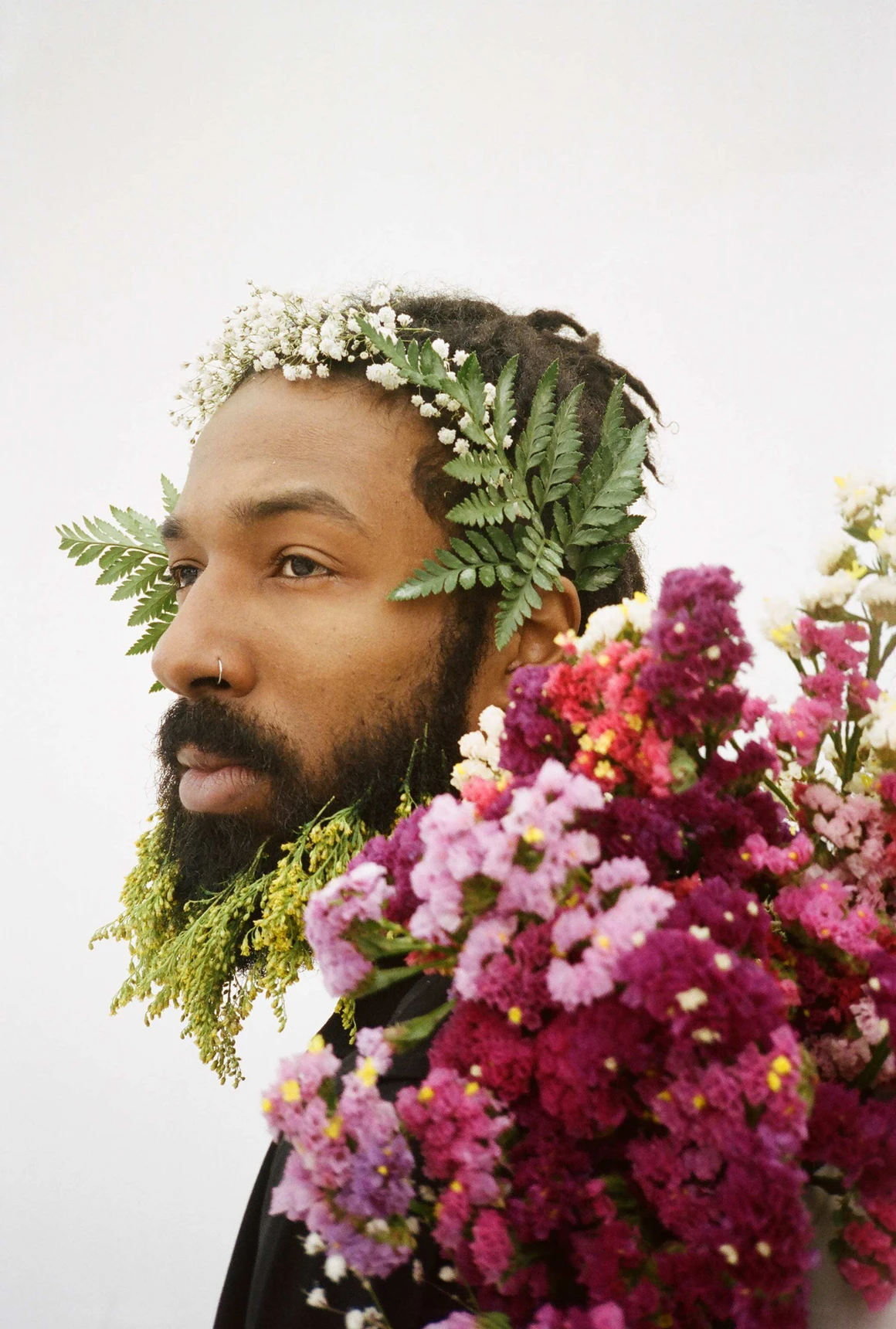 A bearded Black man, adorned with leaves and flowers, gazes off into the distance
