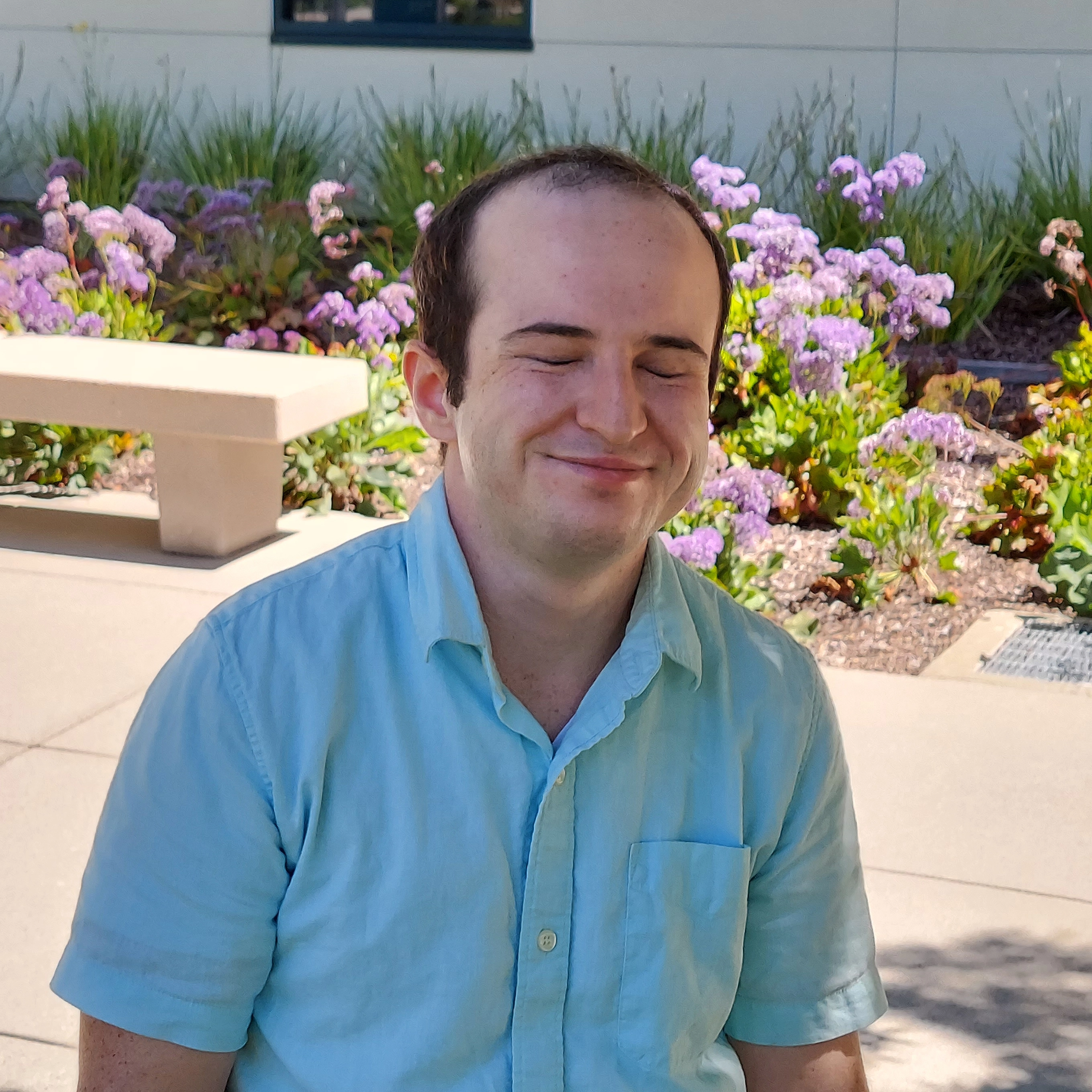 Quentin smiling in an amused way with zir eyes closed.