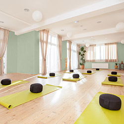 Bright yoga studio with green walls,  yellow mats and black cushions arranged neatly on wooden floor.