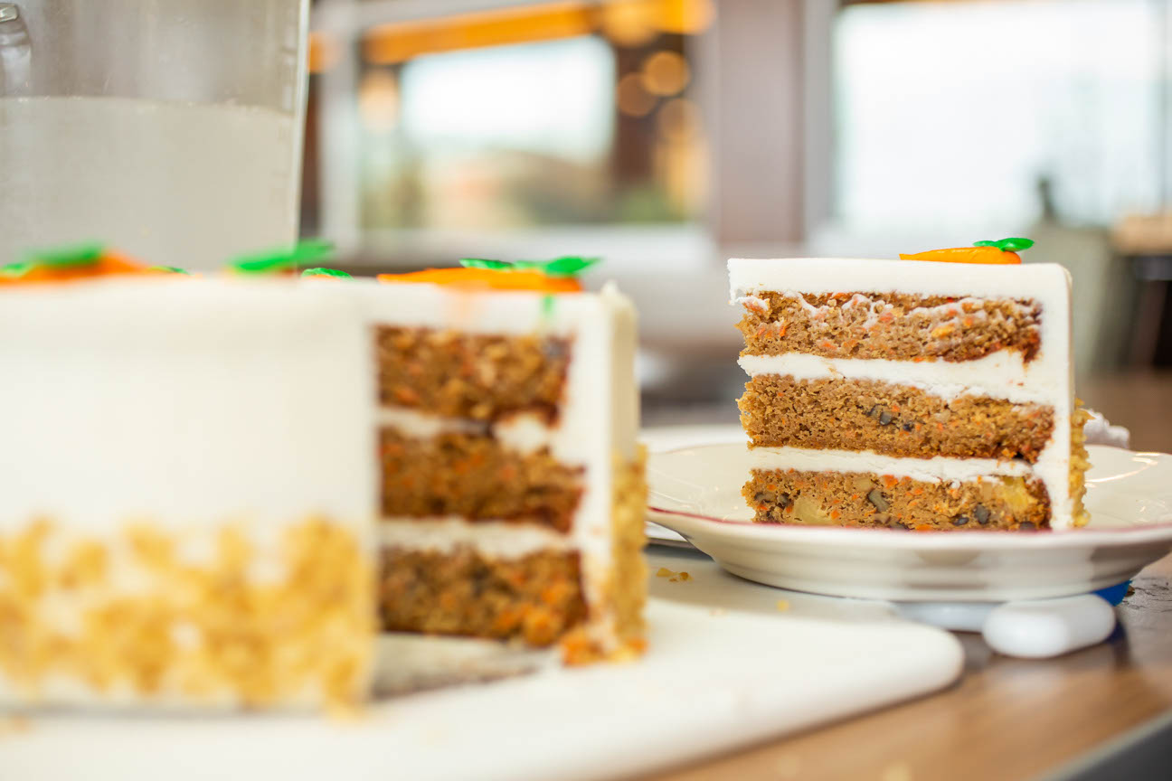 A LARGE CARROT CAKE WITH WALNUTS AND IT HAS  A PEICE BEING TAKEN OUT OF IT.
