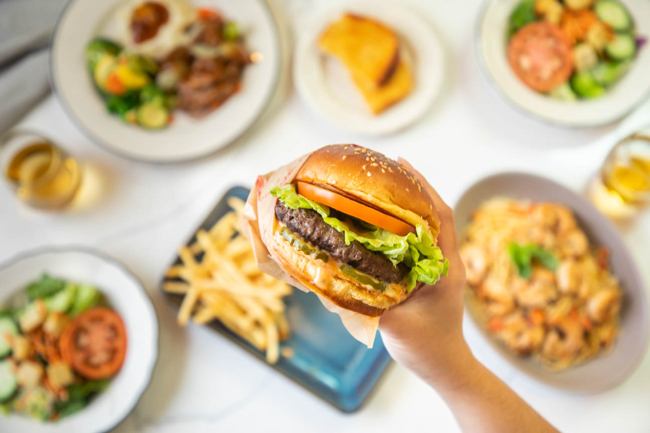 A big hamburger with tomatoes pickles and lettuce being held with one hand. 