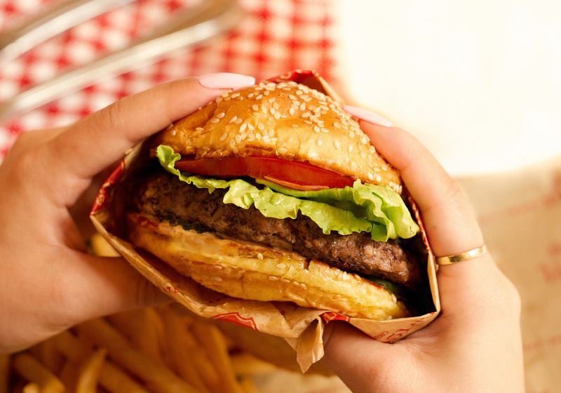 A PERSON IS HOLDING A HAMBURGER WITH TOMATO LETTUCE AND PICKLES ON A SEASAME SEED BUN. 