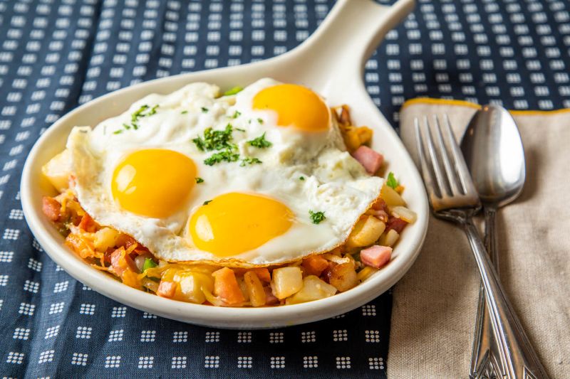 A WHITE BLACK RIMMED PLATE WITH A OMLETE WITH HAME CHEESE AND GREEN BELLPEPPER. ON THE SIDE OF THE OMLETE IS WATERMELON AND CANTALOUPE. BEHIND THAT PLATE IS A SMALL PLATE WITH A MUFFIN.