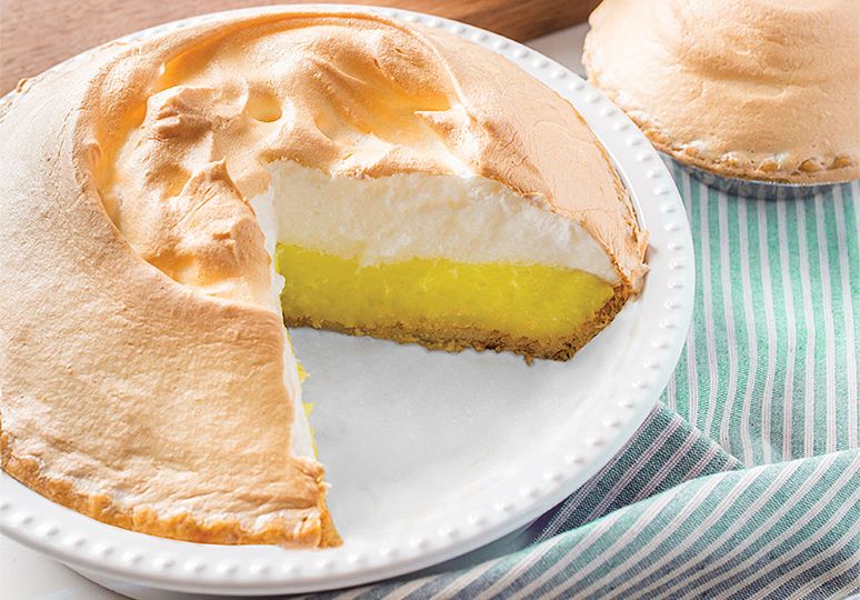 A small plate that has a large piece of Apple Pie. In the background you can see the whole pie that the piece came from. 