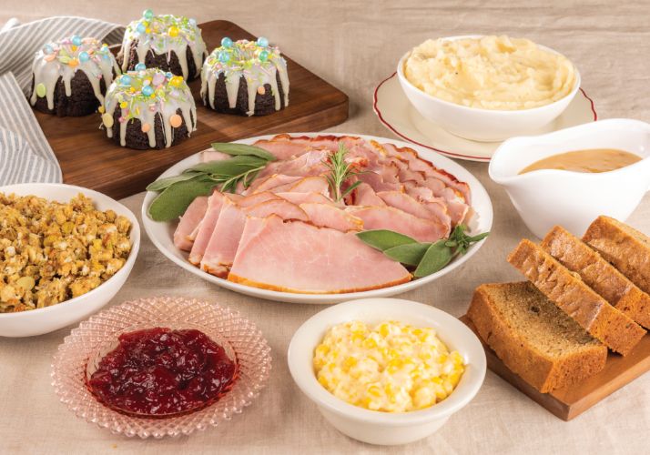 A large berry pie with a piece cut out of it. Fresh Berries on the side along with 2 silver forks and a wooden rolling pin. 