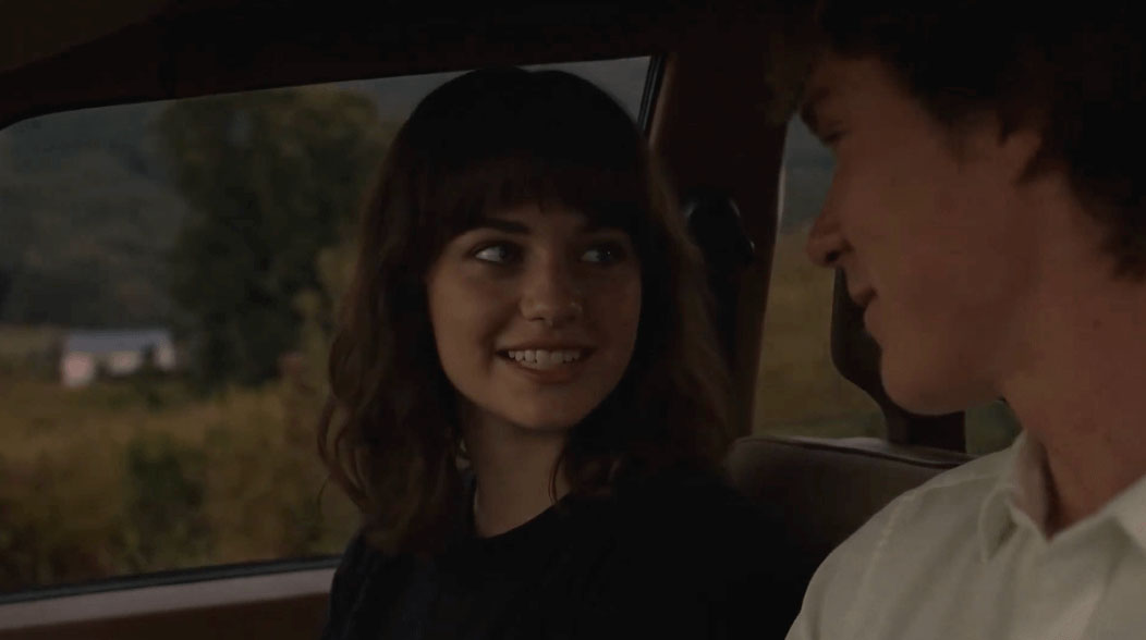 Woman looking over at a male sitting in the drivers seat of a car from the passenger's side smiling