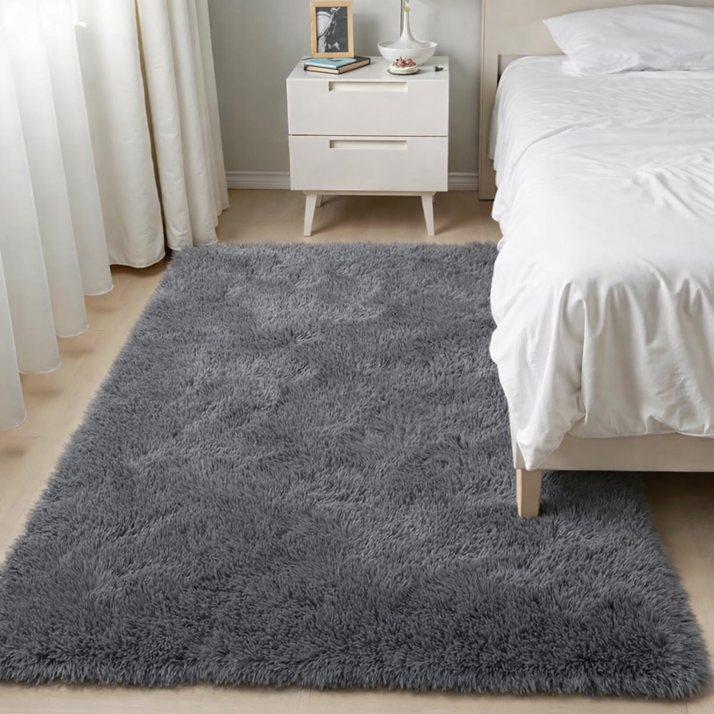 Gray plush shag area rug placed beside a white bed and nightstand in a minimalist bedroom