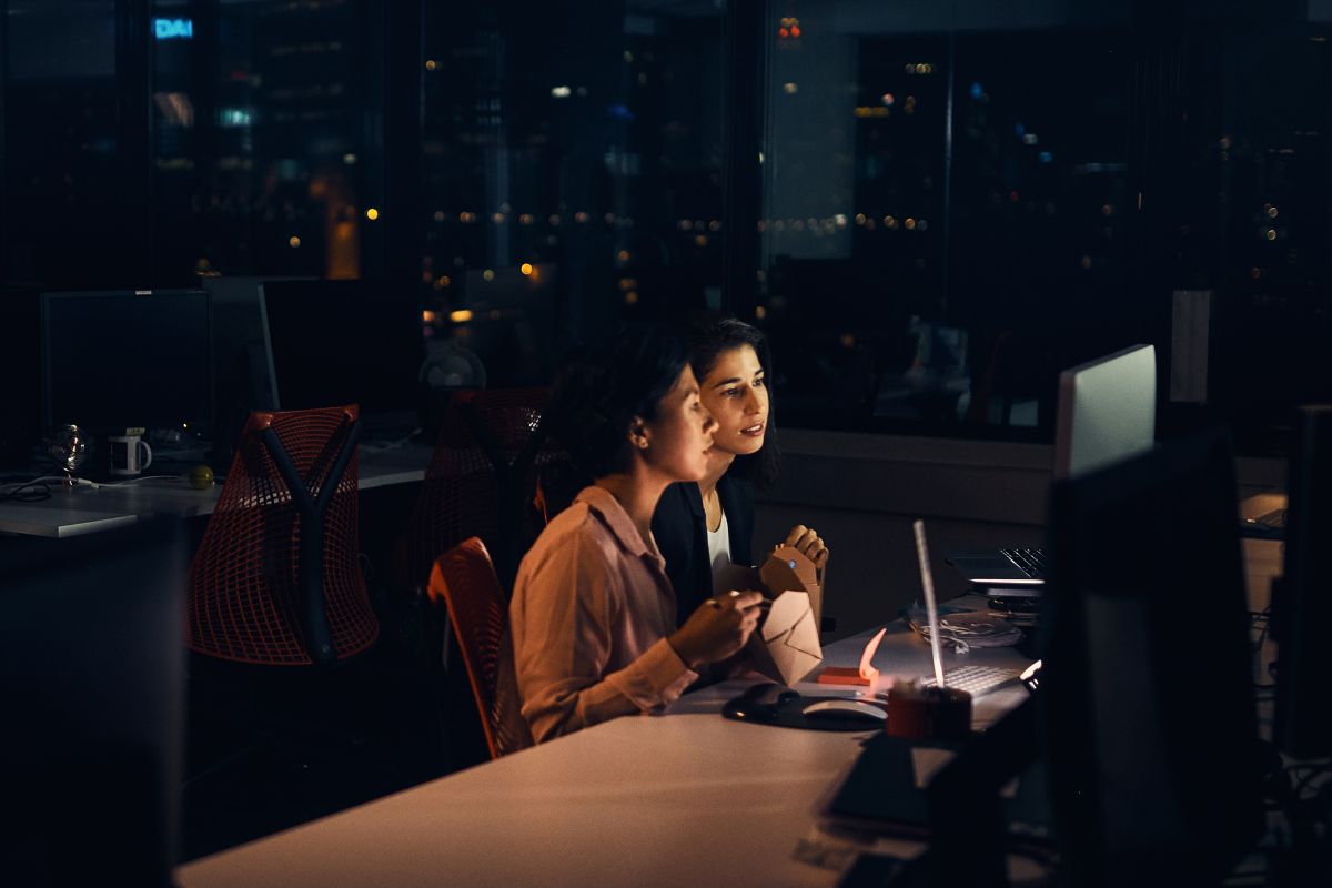 Two people in a dark office looking at a computer screen working late