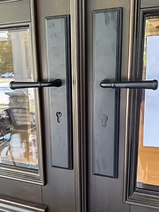Close-up of two dark brown wooden doors with horizontal black door handles and keyholes.