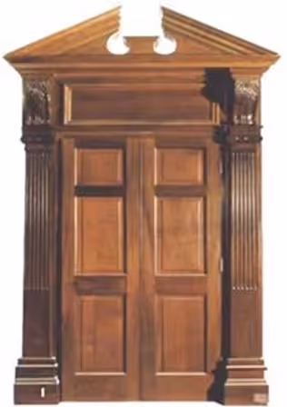 Ornate wooden double door with fluted columns and a decorative triangular pediment on top.