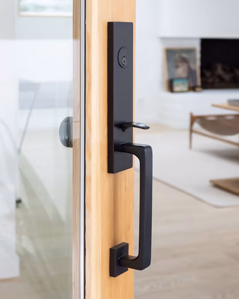 Close-up of a modern black door handle and lock on a wooden framed glass door with a blurred interior background.