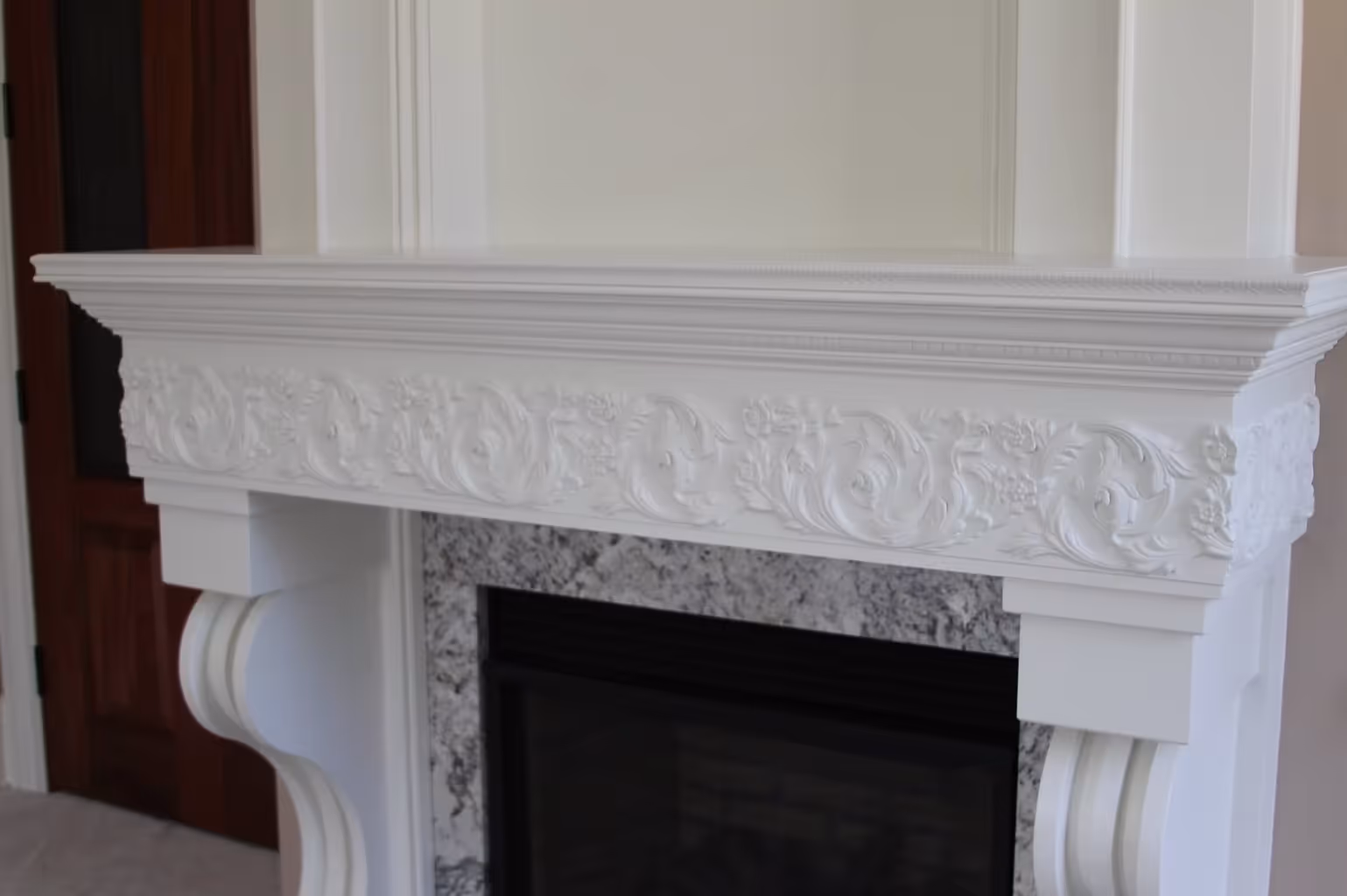 White ornate fireplace mantel with detailed floral carvings and granite interior surround.