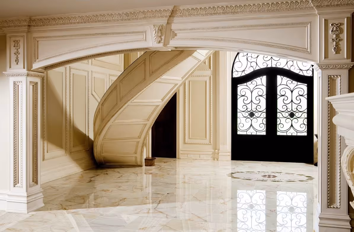 Elegant interior with a curved staircase, ornate molding, and glossy marble floor reflecting a decorative wrought iron door.