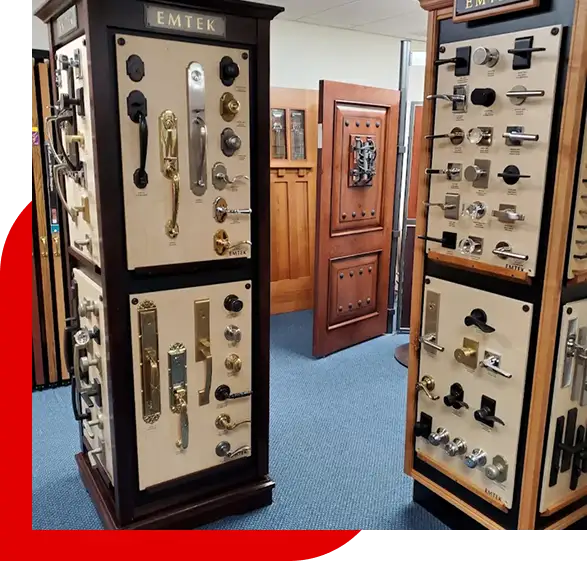 Display stands showcasing various door hardware including handles, knobs, and locks in a showroom with wooden doors in the background.