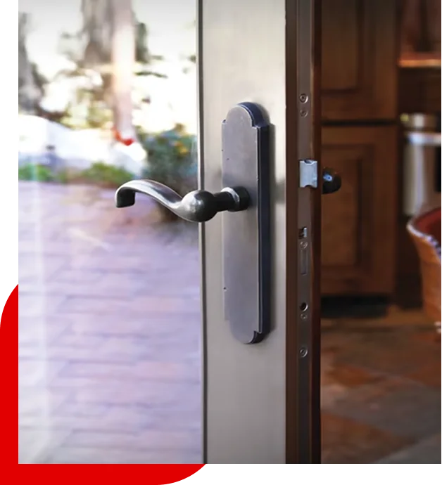 Close-up of a modern metal door handle on a glass door slightly open, with a blurred outdoor patio and indoor kitchen background.