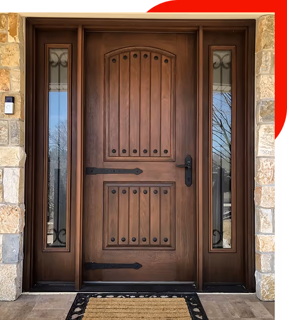 Brown wooden front door with black hardware and two narrow glass panels on each side, framed by stone walls and a doormat in front.