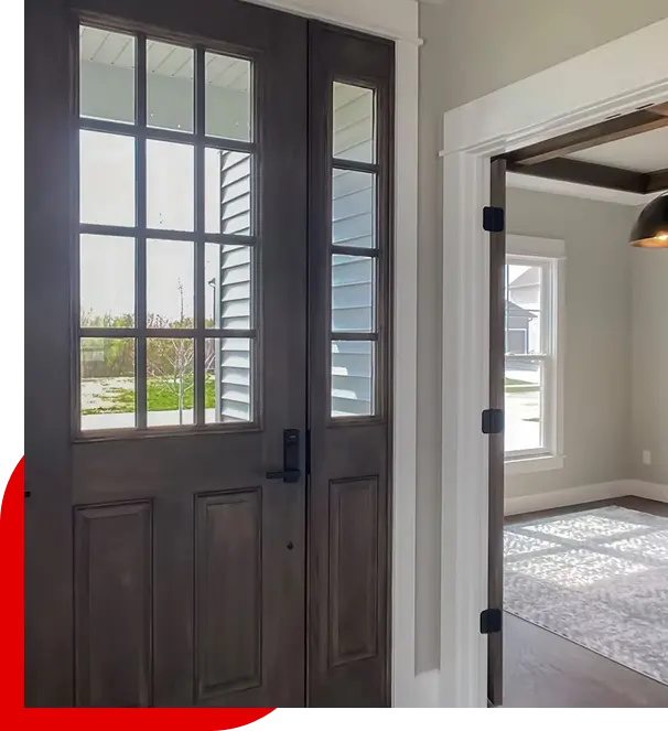 Dark wooden front door with glass panes beside an open doorway leading to a sunlit room with a window and carpet.